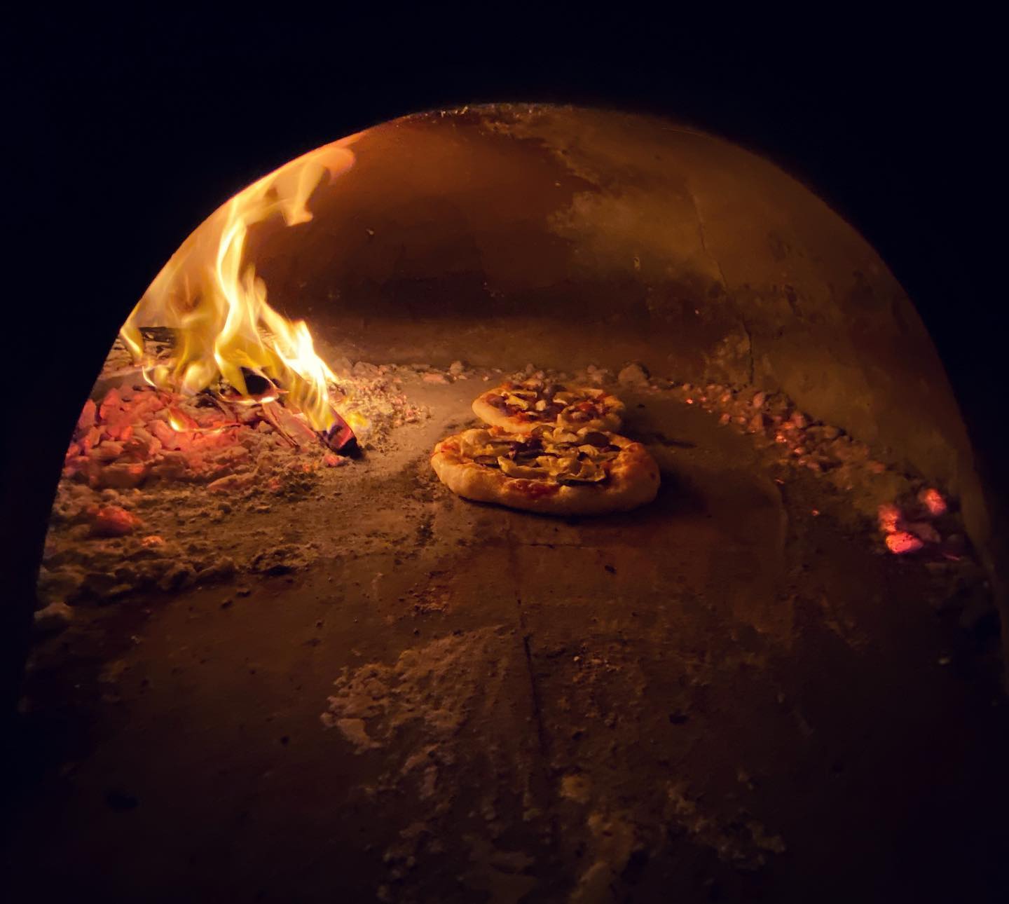 Pizzas in 'n houtvuuroond langs oop vlamme