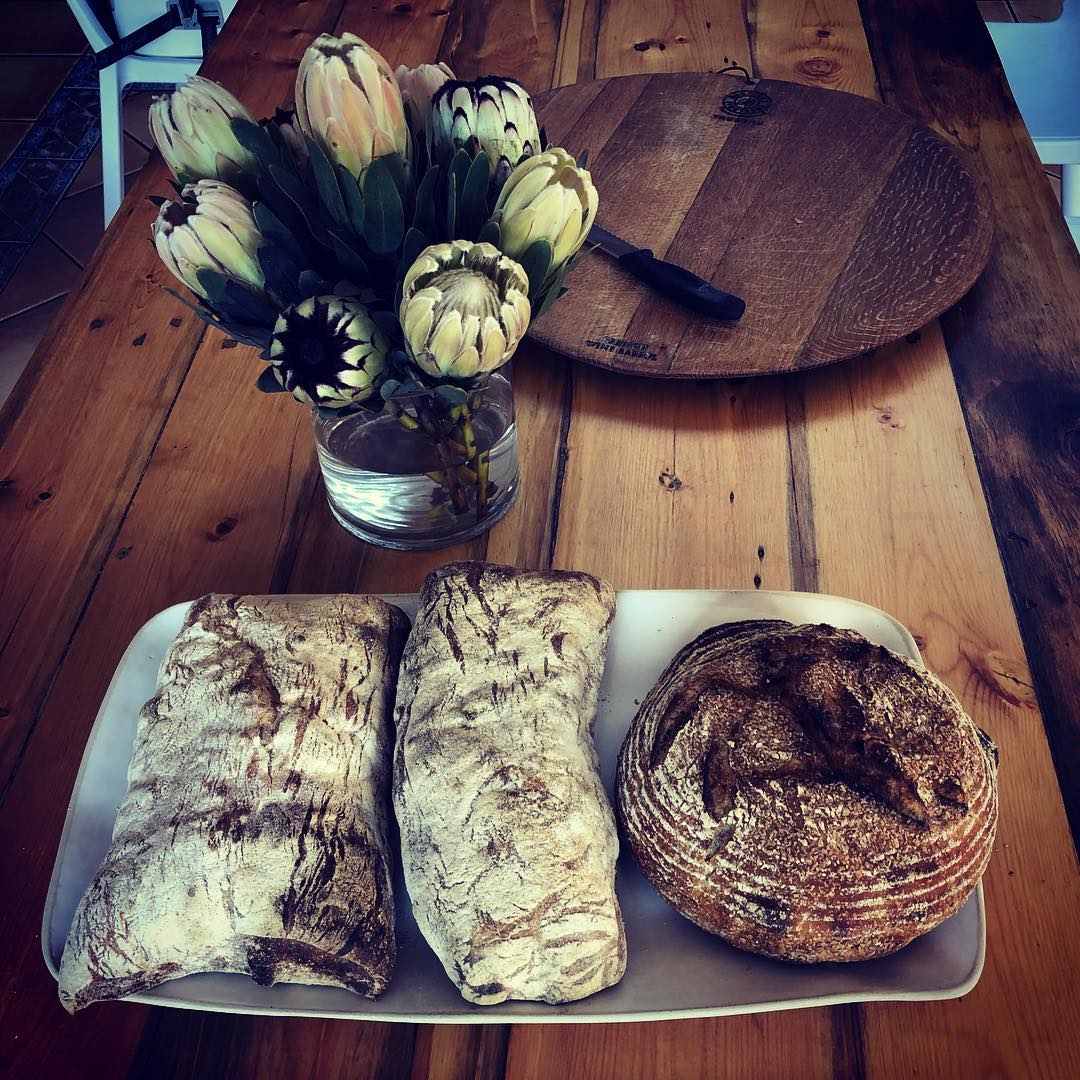 Twee ciabattas en 'n boule op 'n skottel langs proteas